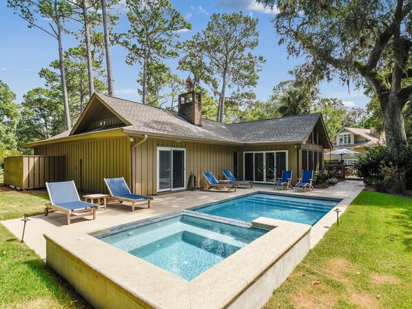 Une maison avec une piscine, des chaises longues et un patio couvert.
