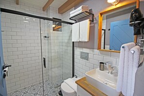 A bathroom with a glass-enclosed shower, white tiled walls, a sink with a wooden countertop, and a mirror with a towel hanging on it. - Bozcaada Teras Otel (Bozcaada)