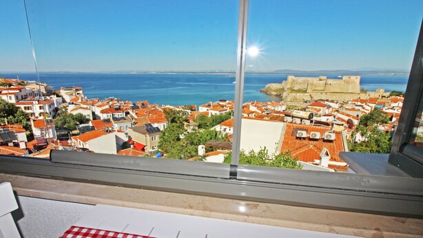 A balcony with a red and white checkered tablecloth, overlooking a coastal town with red-roofed buildings and a historic fort. - Bozcaada Teras Otel (Bozcaada)