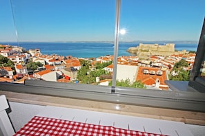 A balcony with a red and white checkered tablecloth, overlooking a coastal town with red-roofed buildings and a historic fort. - Bozcaada Teras Otel (Bozcaada)