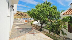 A courtyard with a paved walkway, a tree, and a white building with a tiled roof. - Bozcaada Teras Otel (Bozcaada)
