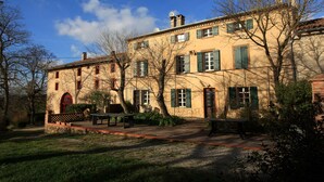 Un bâtiment à deux étages doté d’une cour intérieure, caractérisé par une façade en pierre, des volets verts et une porte rouge.