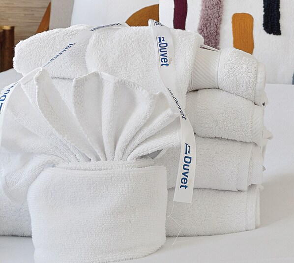 A stack of white towels with 'Duvet' branding, neatly arranged on a bed.