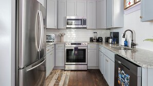 Una cocina moderna con electrodomésticos de acero inoxidable, armarios blancos y piso de madera.