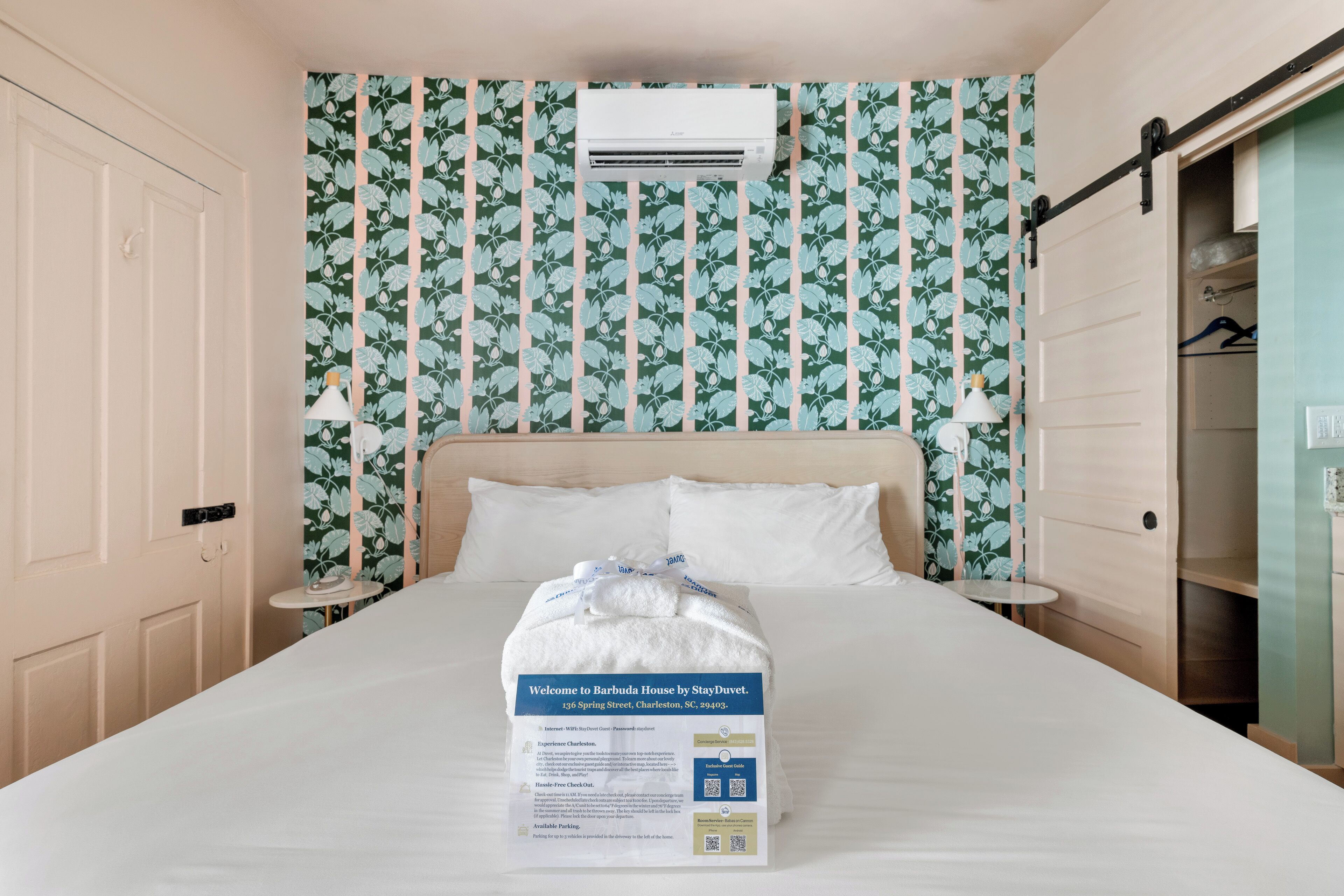 A hotel room with a bed, a bedside table, a lamp, a wardrobe, and a wall air conditioner.