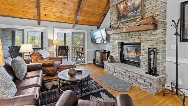 A cozy living room with a stone fireplace, leather sofa, and a television mounted on the wall. - Smoky Mountain Cabin with Stunning National Park Views (Gatlinburg)