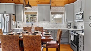 A kitchen with wooden ceiling beams, white cabinets, a dining table with patterned chairs, and modern appliances. - Smoky Mountain Cabin with Stunning National Park Views (Gatlinburg)
