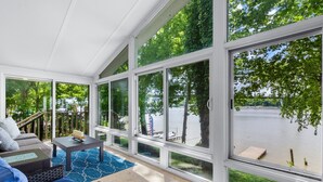 A sunlit room with large windows, a sofa, a coffee table, and a view of a lake. - Riverfront Home on the Ohio River, Private Dock, Hot Tub, Sleeps 8 (Prospect)
