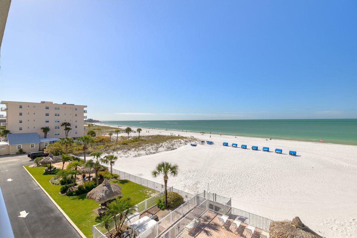 A beach view from a balcony with a hotel building, beach umbrellas, and lounge chairs.