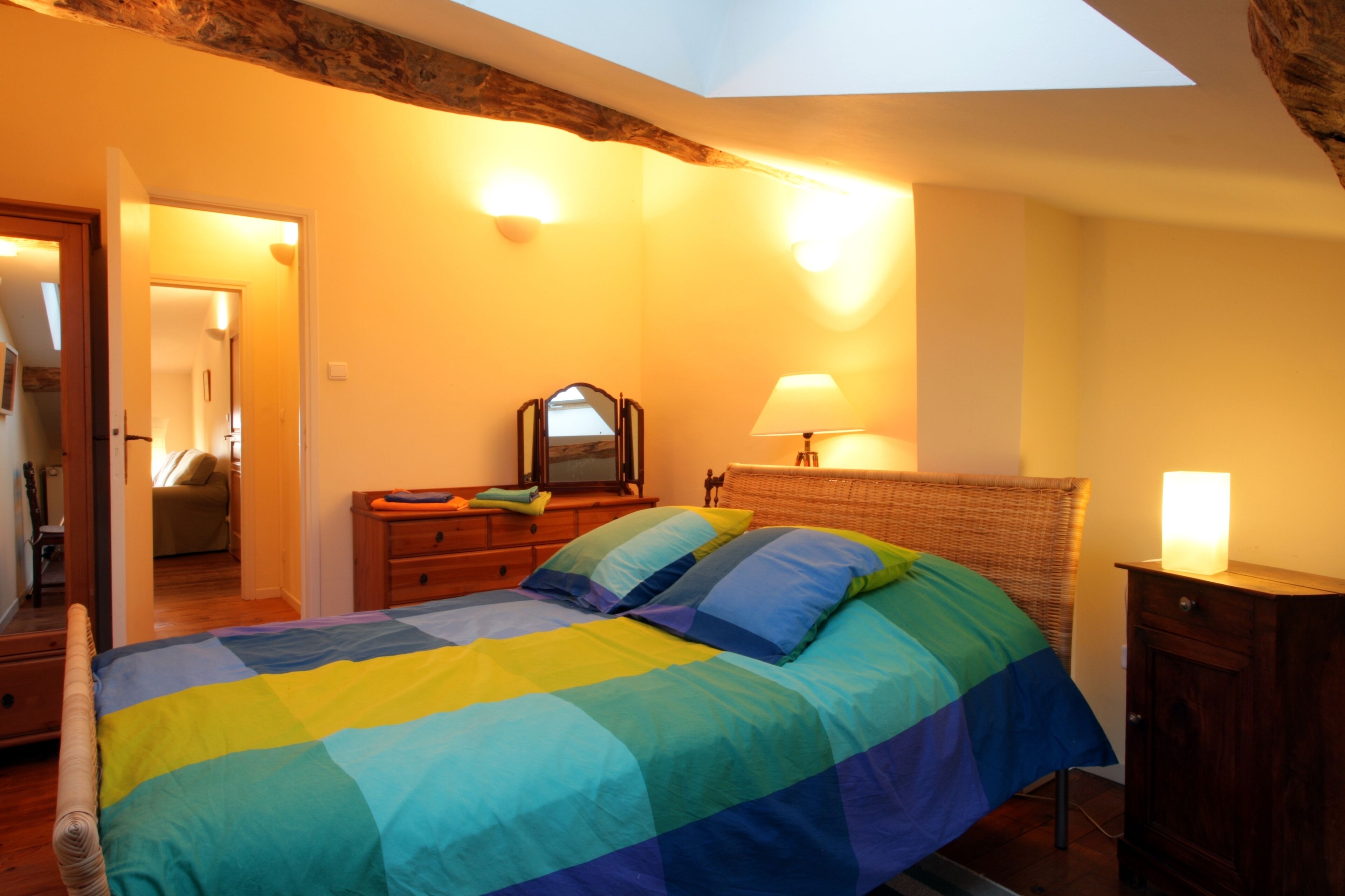 A bedroom with a bed, a dresser, a mirror, and a skylight.