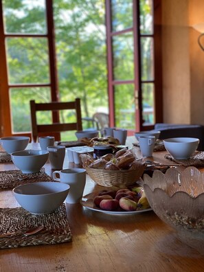 A breakfast table with bowls, cups, and a basket of bread and fruit. - Artists' House in the Countryside—View of the Pyrenees (Saint-Félix-de-Tournegat)