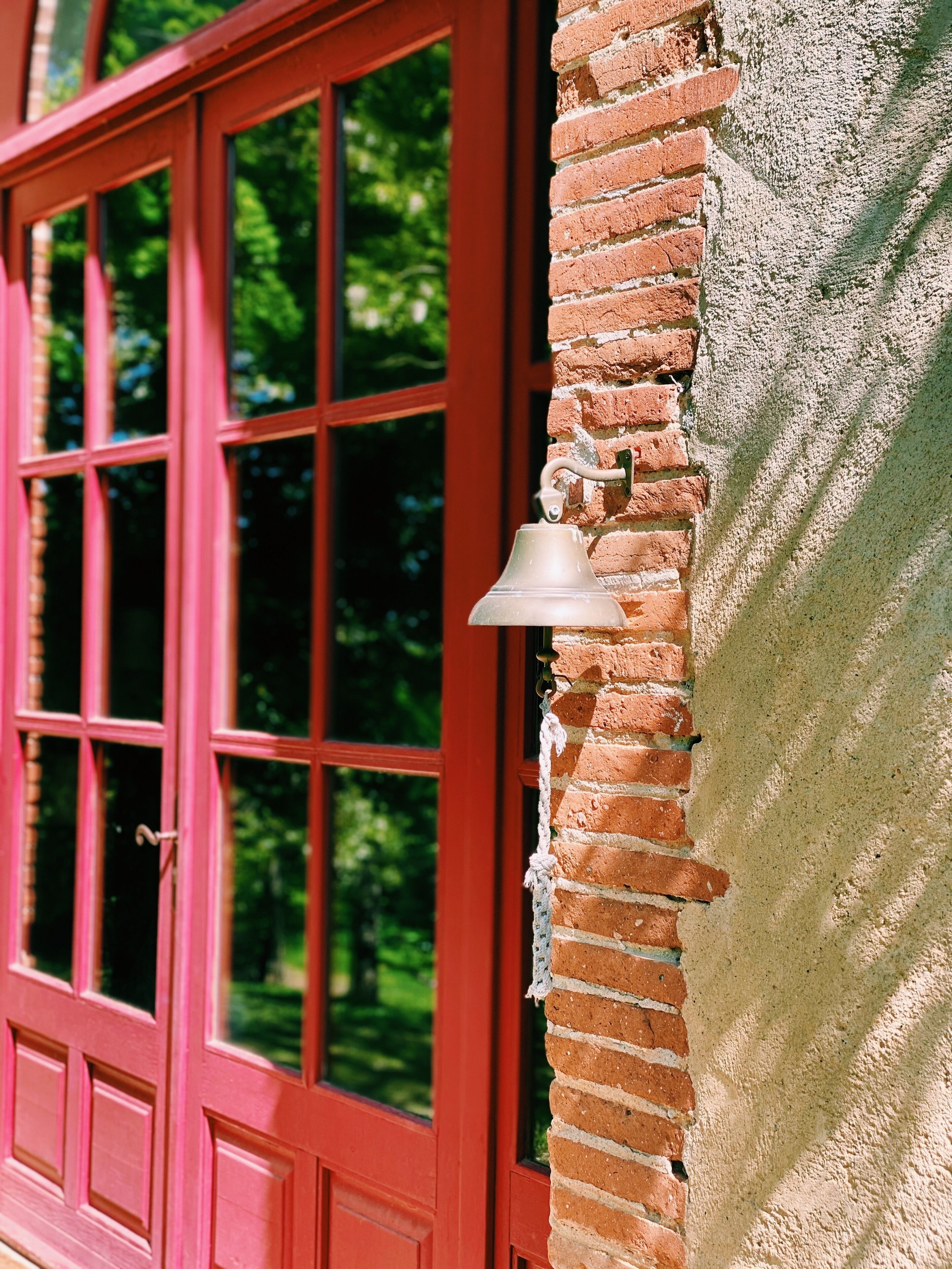 Une fenêtre rouge avec une cloche fixée à un mur de briques.