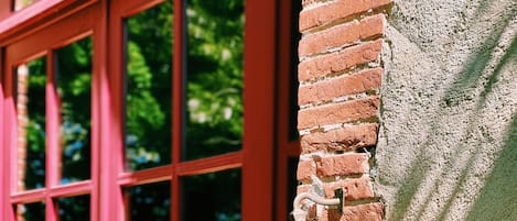 Una ventana roja con una campana unida a un muro de ladrillo.