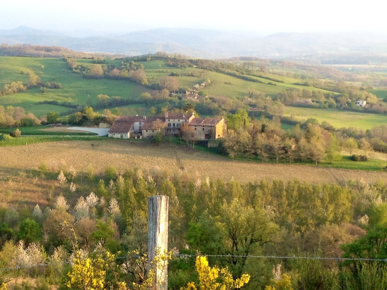 A rural landscape with a farmhouse surrounded by fields and hills.