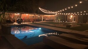 A swimming pool with string lights, a covered patio, and a lawn area.