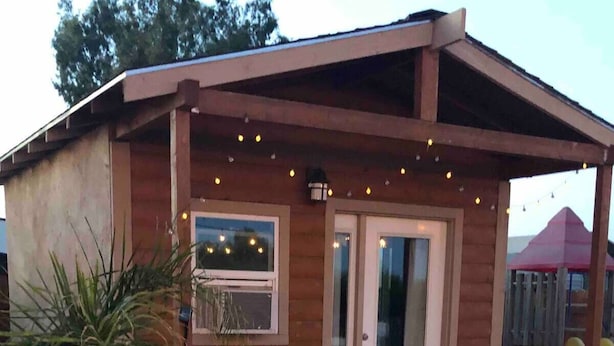 A wooden house with a covered patio, a table and chairs, and a small garden.