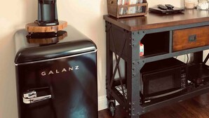 A compact kitchen area with a Galanz espresso machine, a coffee maker, a TV mounted on the wall, and a wooden cabinet with a DVD player and books.