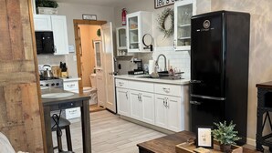 Una cocina moderna con armarios blancos, un refrigerador negro y una zona de comedor con una mesa de madera y un sofá de cuero negro.