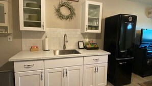 Una cocina moderna con armarios blancos, un lavamanos de acero inoxidable y un refrigerador negro.