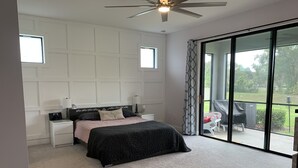 Een slaapkamer met een bed, nachtkastjes, een plafondventilator en een schuifdeur naar een terras.