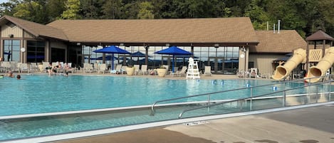 A swimming pool with lounge chairs and umbrellas, a lifeguard stand, and a slide.