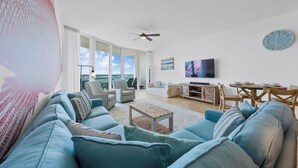 En moderne stue med en stor sofa, et sofabord og et fjernsyn. Der er et spiseområde med et bord og stole.