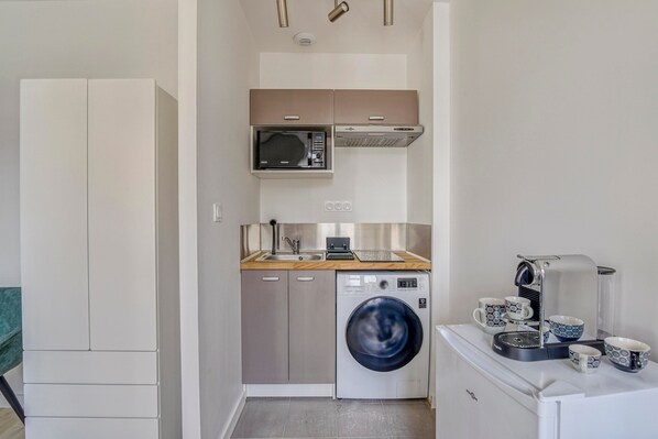 A compact kitchen with a washing machine, microwave, and coffee maker.