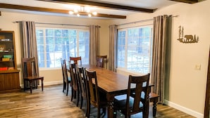 Ein Esszimmer mit einem großen Holztisch, Stühlen, zwei Fenstern mit Vorhängen und einer Kristallleuchter.