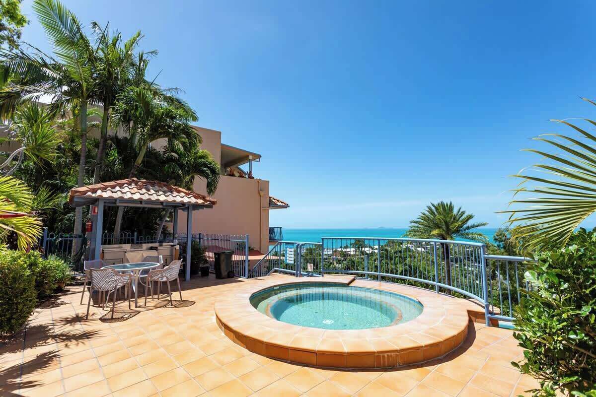 A pool area with a hot tub, outdoor seating, and a view of the ocean.