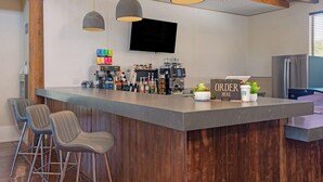 Ein moderner Barbereich mit einer Theke, Barhocker, einem Fernseher und einer Kaffeemaschine.