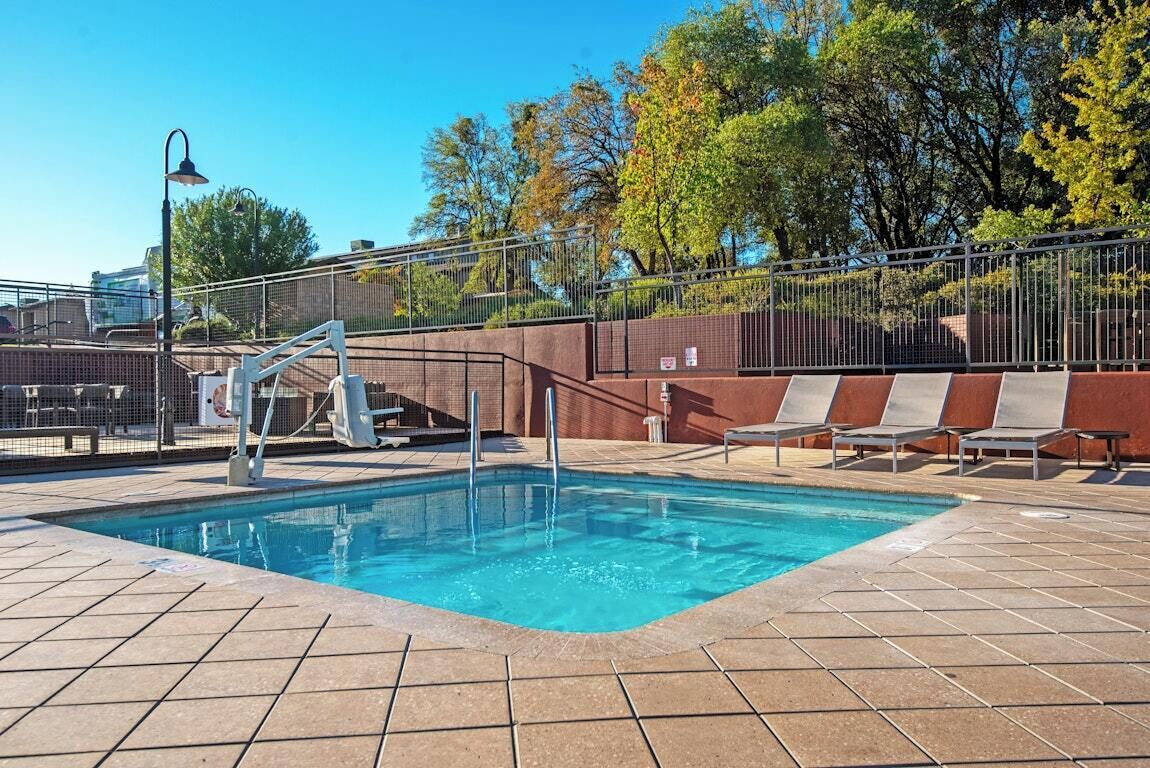 A swimming pool with a metal ladder, lounge chairs, and a fence.