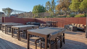 Una terrassa exterior amb taules i cadires de fusta, un sofà i una xemeneia.
