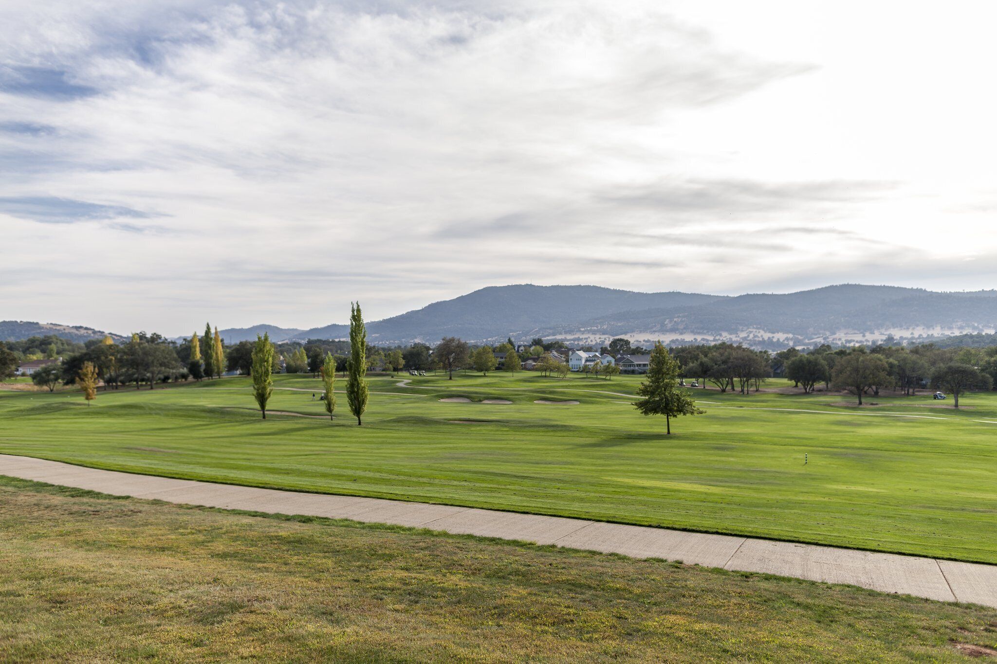 Un campo de golf con un camino despejado, árboles y montañas a lo lejos.