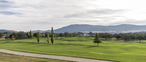 Un campo de golf con un camino despejado, árboles y montañas a lo lejos.