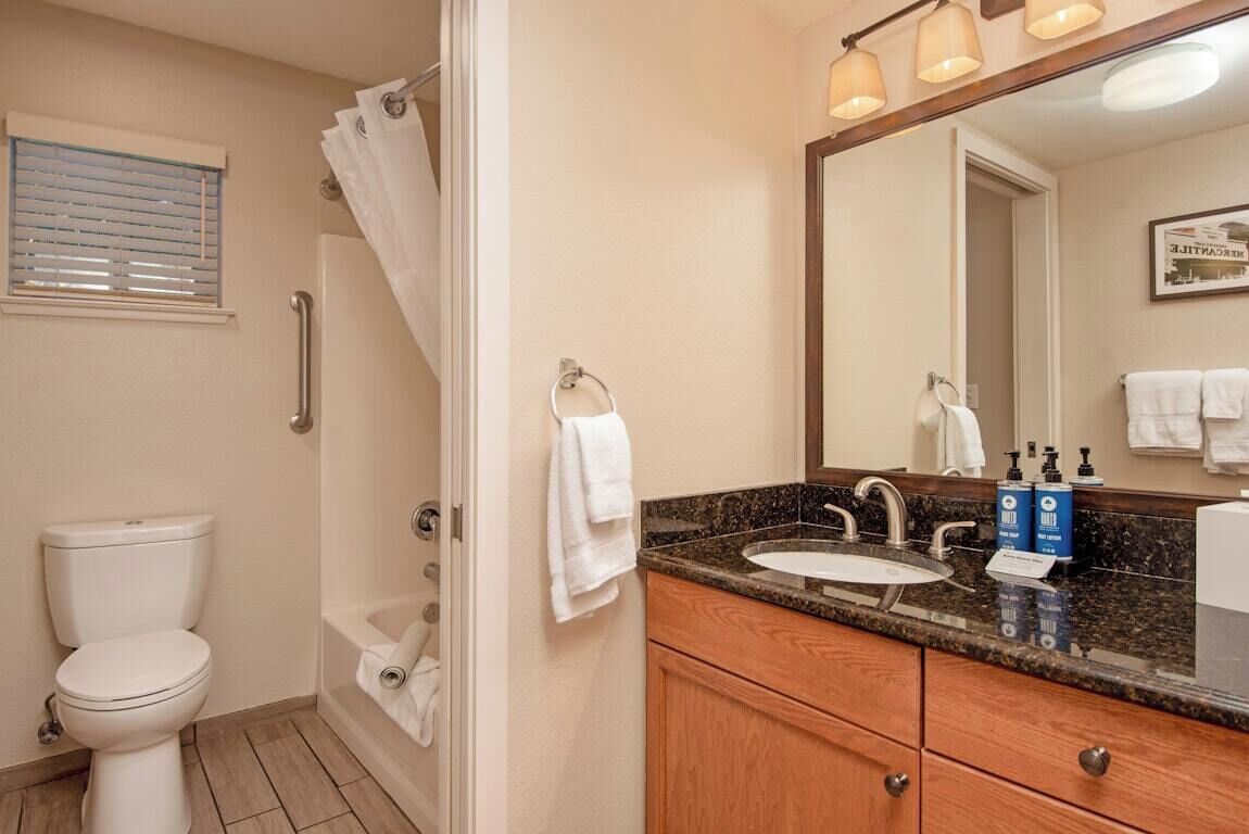 A bathroom with a toilet, shower, sink, and mirror.