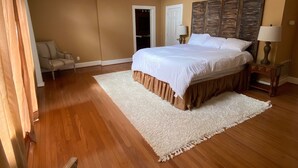 Un dormitorio amplio con una cama grande, un ventilador de techo, piso de madera y una silla.