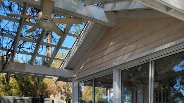 Un patio techado con mobiliario exterior, un ventilador de techo y vistas del paisaje circundante.