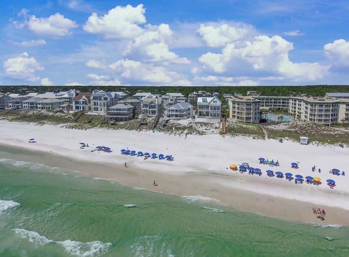 A beachfront hotel with multiple buildings, a sandy beach with umbrellas, and ocean waves.