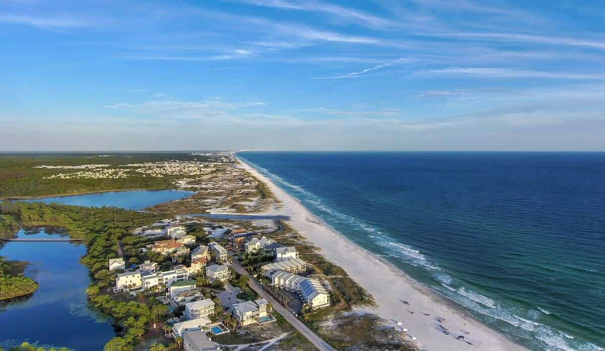An aerial view of a coastal area with a beachfront hotel, a marina, and a bridge connecting to the mainland.