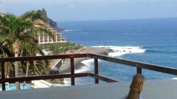 Ein Tisch mit einer Champagnerflasche, einem Glas und einer Blume, mit Blick auf einen Strand und das Meer.