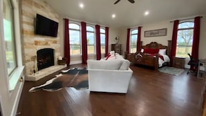 A spacious living room with a fireplace, a white sofa, a wooden bed, and large windows with red curtains. - NEW Hacienda Ranch W/ Resort Style Pool (Hempstead)