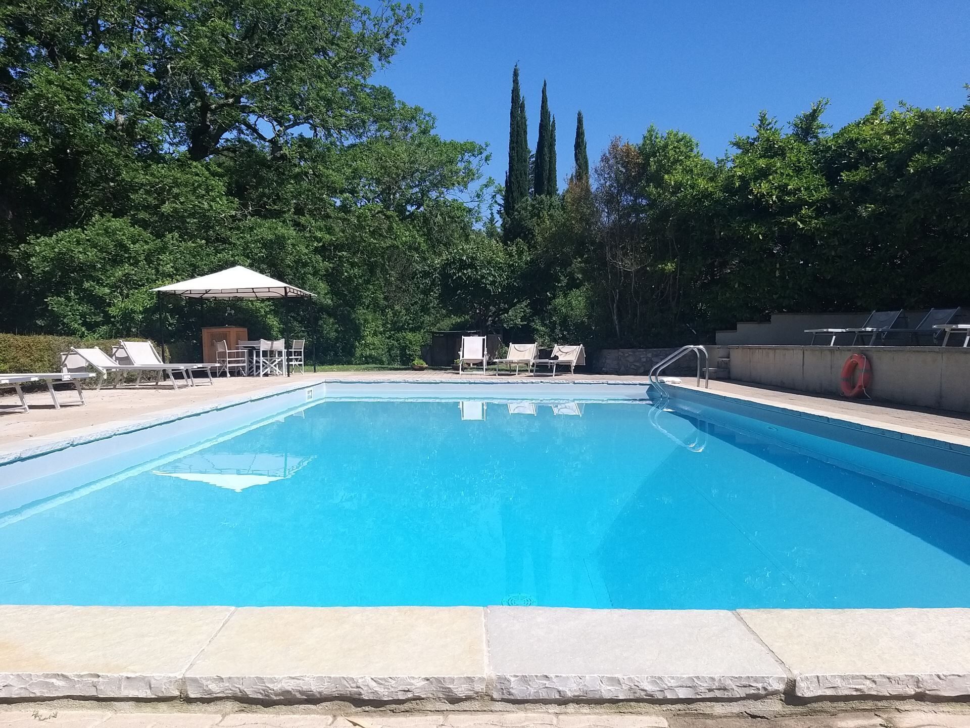 Una piscina rectangular con agua azul cristalina, rodeada de sillas de descanso y una zona de estar techada.