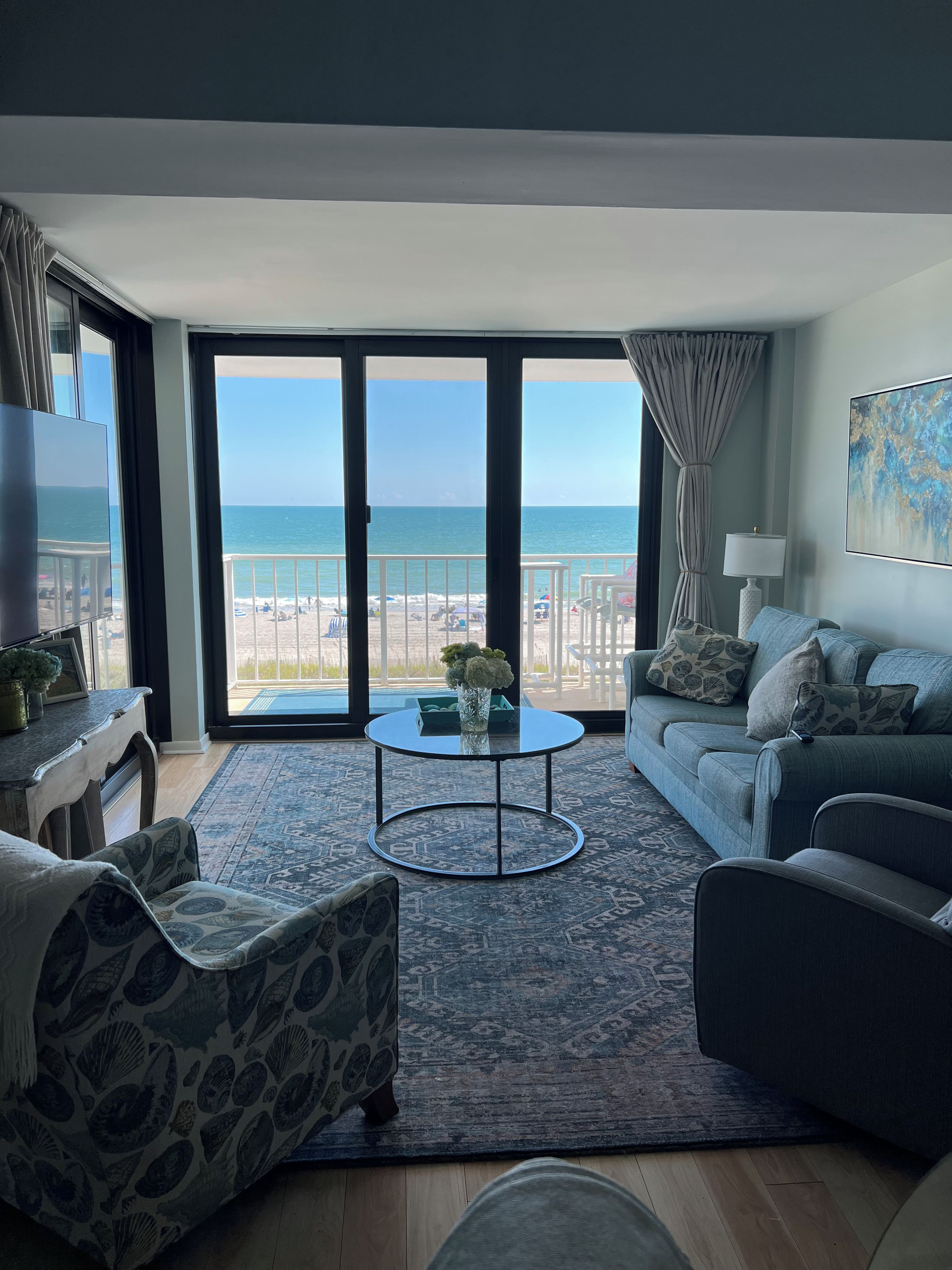 A living room with a view of the beach, a round coffee table, and a sofa.