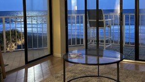 Una habitación con una mesa y sillas de vidrio, vista al océano y un balcón con barandilla.