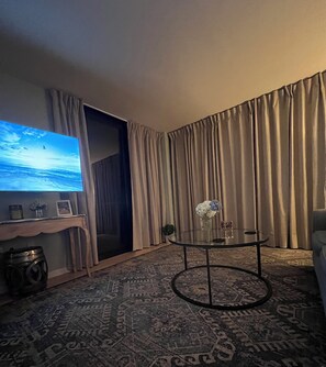 A room with a large flat-screen TV, a round glass coffee table with a vase, a patterned rug, and a sofa. - Gorgeous, unobstructed direct oceanfront views!!! New floor to ceiling sliders! (North Myrtle Beach)