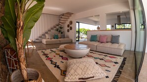 A modern living room with a large plant, a white sofa, a coffee table, and a staircase. - Fully equipped villa for 6 to 8 people located in Lajares (Lajares)