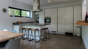 Una cocina moderna con una isla grande, taburetes de bar, horno empotrado y una ventana que muestra follaje en el exterior.