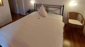 A bedroom with a large bed, two bedside lamps, a wicker chair, and a door leading to another room.