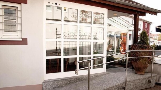 A hotel entrance with a glass door, a metal railing, and a large potted plant.