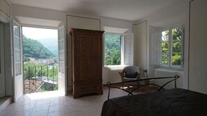 Een slaapkamer met een bed, een houten garderobe, een stoel en uitzicht op groen door een raam.